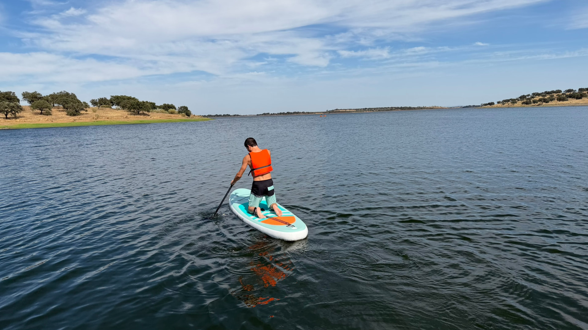 Praticante de stand up paddle no Grande Lago Alqueva com colete salva-vidas laranja